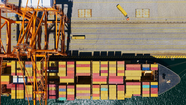 Cargo ship loading and unloading colorful freight containers at a bustling port terminal from an aerial view, showcasing global logistics and supply chain operations