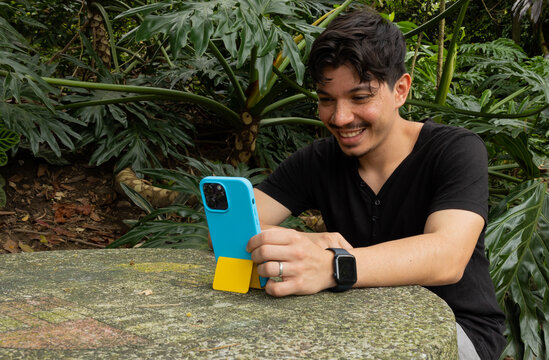 Freckled young man sitting at a park table attentively looking at his mobile phone. Entertainment, digital communication, social media, and leisure time concept