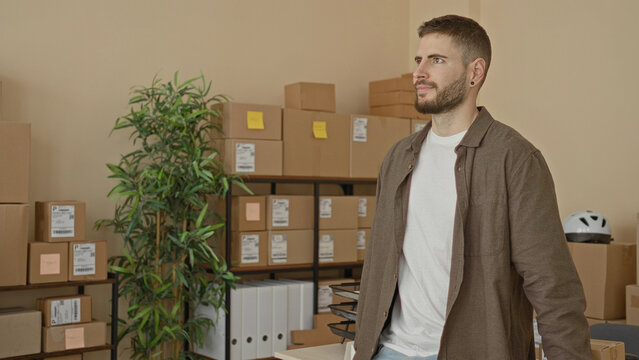 Man with cardboard boxes and crossed arms standing at packing desk in building; confidence entrepreneurship.