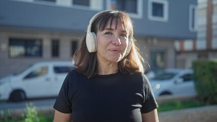 Woman wearing white headphones waves hand and mouths along to music on a sunny street in front of a building and parked van  listening contentment. © Krakenimages.com