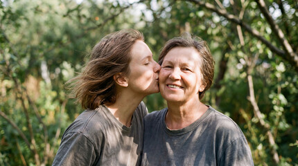 Fototapeta premium A heartwarming lifestyle shot of a young adult daughter giving her smiling senior mother a tender kiss on the cheek. 