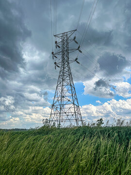 Dark storm clouds over a rural field by a high voltage electricity transmission tower in the American midwest