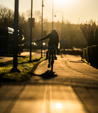 Cyclist signaling turn while riding on suburban bike path in warm sunrise light.
