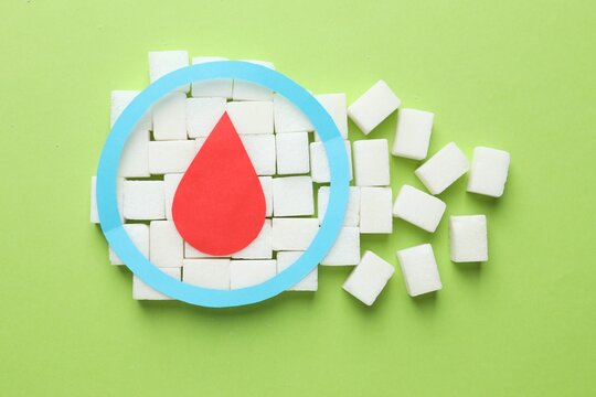 Diabetes. Sugar cubes, paper blood drop and circle on green background, flat lay
