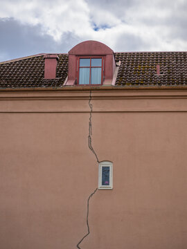 Cracked plaster building facade with small window and roofline.