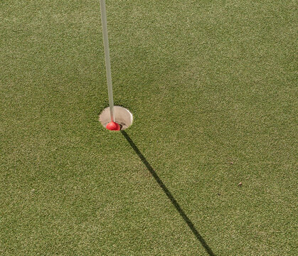 Red golf ball partially inside hole on green.