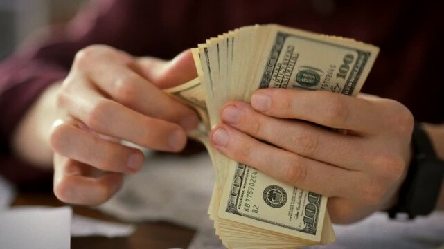 An accountant sits at a table, carefully counting money and inspecting each note. This precise routine highlights the principles of saving, accumulation, and proper fund distribution in finance