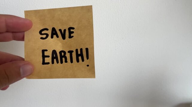 Hand holding kraft paper sign with handwritten Save Earth message on white background