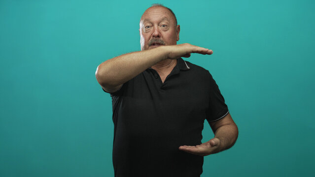 Man in black polo shirt holds forearm across face and cupped hand measuring a height in studio; thoughtful measurement.