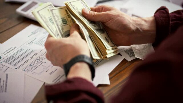 At cluttered desk, an aspiring entrepreneur tallies cash and bills, tapping a calculator to map out expenses and allocate capital, embodying the finance planning essential to launching a new business