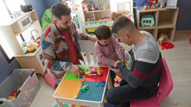 Man guiding little boy stacking colorful building blocks on a play table in a building; playful family bonding.
