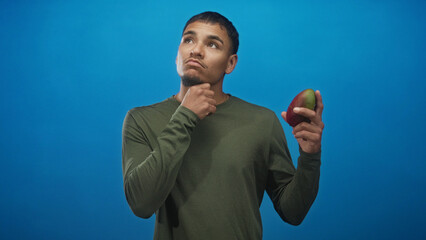 Obraz premium Man holding mango with hand on chin in studio, inspecting the fruit and weighing ripeness and flavor options; thoughtful choice.