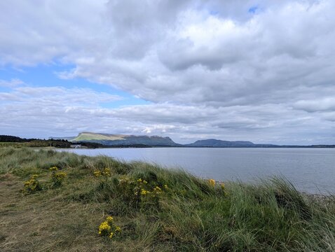 Coastal view in Ireland featuring grassy sand dunes in the foreground and the distinctive flat-topped Benbulben mountain in the distance.