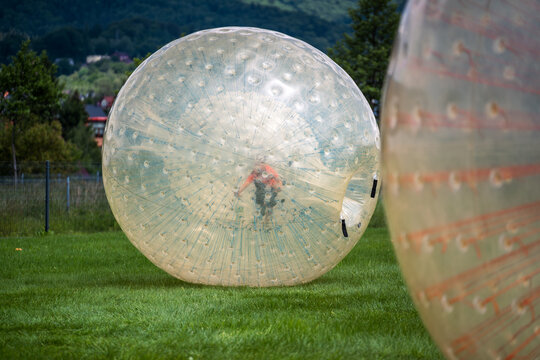 Active child having fun inside a giant inflatable zorbing ball on a green meadow in summer