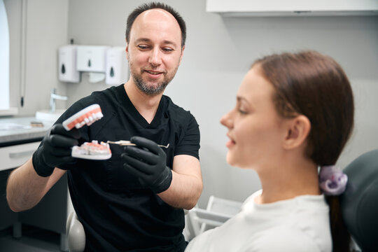 Adult male dentist with dental prosthetics in clinic with female patient