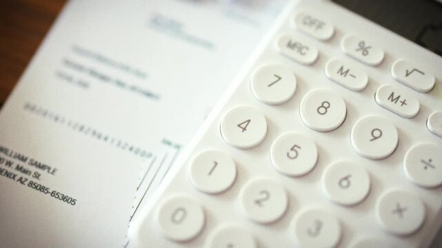 In an office workspace, calculator shows bright digits beside stacked utility bills on desk, emphasizing the routine of calculating amounts and processing payment for services in professional setting