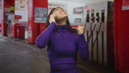 Woman holding smartphone to ear, smiling with clenched fist in celebration at street gas station  triumph joy relief. © Krakenimages.com