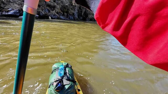 Entering narrow gorge into calmer pool, paddler navigates between rockfaces and boulders, current easing into backwater, concentrated stroke work, dramatic canyon framing and spring light.