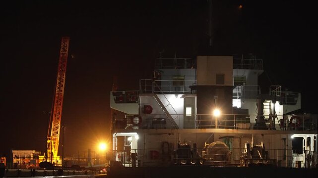 夜の港でオレンジ色の照明に照らされるクレーンと大型船舶の4K動画

