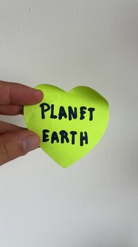 Hand holding green heart shape sign with Planet Earth text