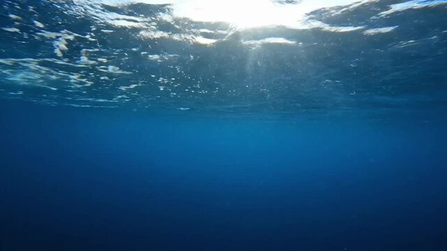 Underwater waves moving and flowing in deep blue ocean water with light shining above