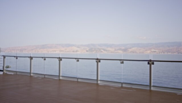 Boat deck with glass railing and distant shoreline softly defocused with shallow bokeh, outdoor; background backdrop copyspace calm.