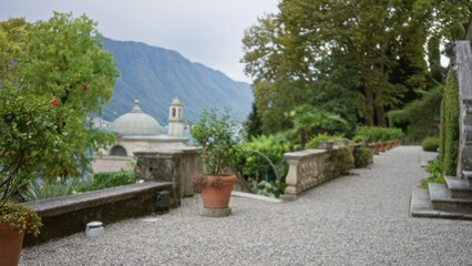 Obraz premium Blurred terrace scene with potted plants, gravel path and distant domed building in soft defocus, garden; background backdrop copyspace calm.