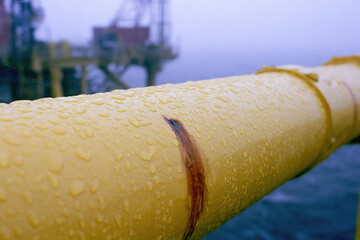 Fototapeta premium Yellow pipe rain droplet rust spot industrial railing offshore rig misty background harsh daylight macro detail metal surface wet texture