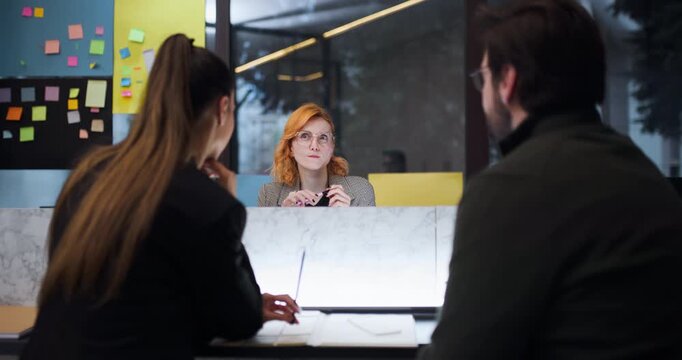 Meeting at the office where a woman gives a presentation to two people about a new project and discusses ideas while they take notes