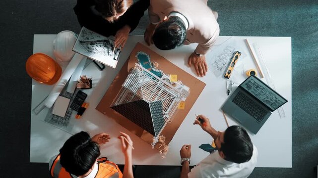 Top down aerial view of smart architect engineer team inspect house model while manager hold blueprint and asking about building construction. Group of diverse engineer working together. Alimentation.