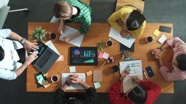 Top view of smart business man standing while writing and presenting marketing idea at whiteboard. Group of diverse happy people looking at stock market chart and listening presentation. Convocation.