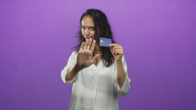 Young hispanic woman holding financial creditcard with palm raised stop gesture in studio; refusal warning.