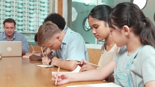 Asian girl laughing at caucasian boy idea while professional teacher teaching about program. Happy diverse student work classwork while sitting at classroom. Creative education concept. Edification