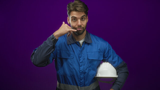 Man construction worker holding white hardhat with hand making callme gesture in studio; confidence.
