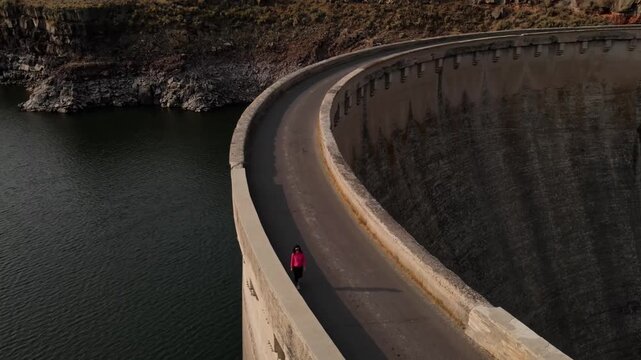 Aerial shot of an Asian woman hiking across the historic 100 year old Salmon Falls Dam in Southern Idaho