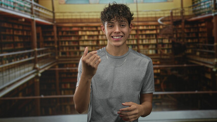Teenage man points finger to camera while smiling amid tall bookshelves in a library building  confidence youth. © Krakenimages.com