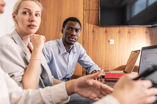 A group of young business people are sitting together in the office, brainstorming ideas and discussing future projects, while taking notes and sharing suggestions.
