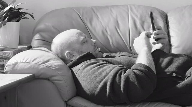Middle-aged white man laying on sofa scrolling and typing on his mobile phone. 
