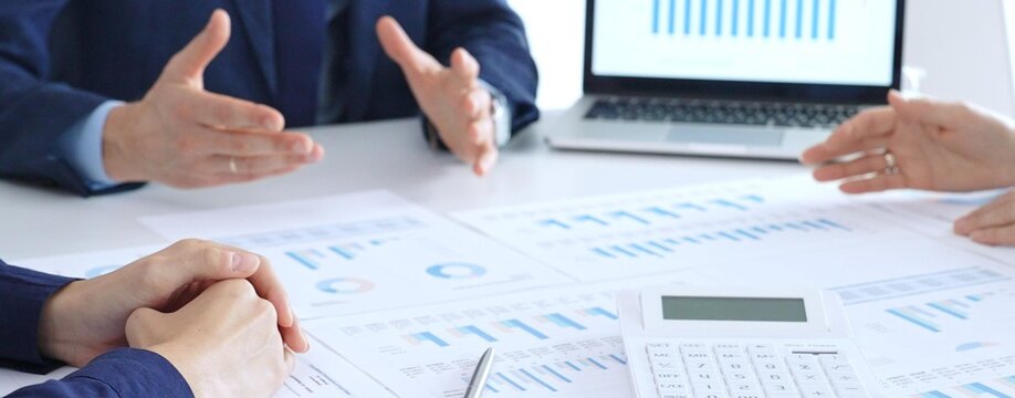 Business professionals collaborating at a conference table, reviewing financial charts and reports, using a laptop and calculator while engaging in discussions about strategy and performance