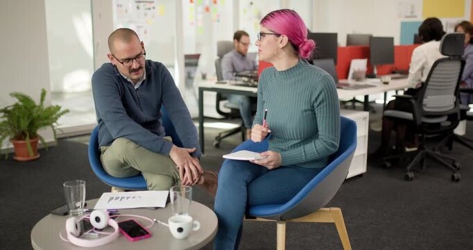 Team members collaborate in an office setting discussing ideas and strategies while seated at a table with notes and a laptop present