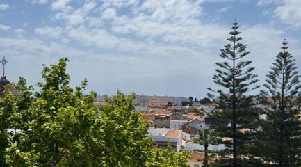 Fototapeta premium Tavira shows white houses and narrow streets from above, highlighting the tow's layout, greenery, and surrounding hills on a clear day in Algarve, Portugal