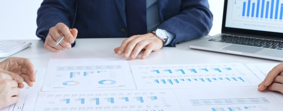 Business people collaborating at a conference table, reviewing financial charts and reports, using a laptop and calculator while engaging in discussions about strategy and performance. Accouters at