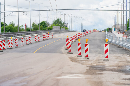 Red and white striped traffic warning barriers line a city bridge road during a lane closure and asphalt resurfacing construction project