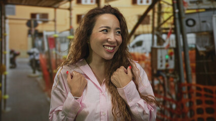 Fototapeta premium Woman in pink shirt shrugs shoulders with palms up at building construction site, smiling toward camera; bemusement.