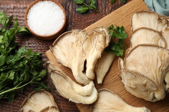 Fresh oyster mushrooms, salt and parsley on wooden table, flat lay