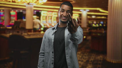Obraz premium Man beckons with bare hand in a casino building, smiling and offering a playful invite toward the slot machines and gaming floor; confident invitation.