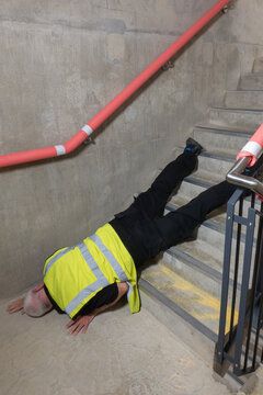 Mature construction worker trips and falls while working on concrete stairs in a new build.  Senior engineer slips and falls down a flight of stairs while surveying a building.
