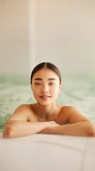 A serene wellness scene captures a relaxed woman immersed in warm water at a minimalist spa. Soft daylight and subtle hues evoke luxury, balance, and tranquility. © Valeri Luzina
