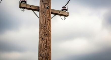 Fototapeta premium Solitary wooden utility pole with insulators against a moody cloudy sky, representing rural power infrastructure and essential services.