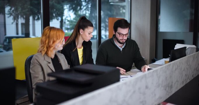 Group of people working together in an office during the day discussing documents and using laptops at a shared workspace